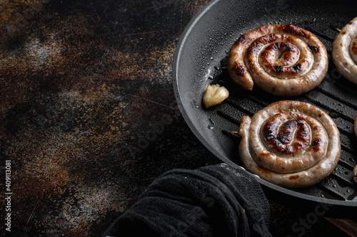 Grilled pork meat sausages in cast iron frying pan, on old dark rustic background , with space for text copyspace