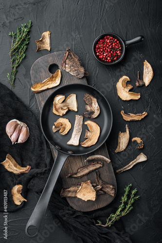 Dried wild mushrooms in cast iron frying pan, on black background, top view flat lay