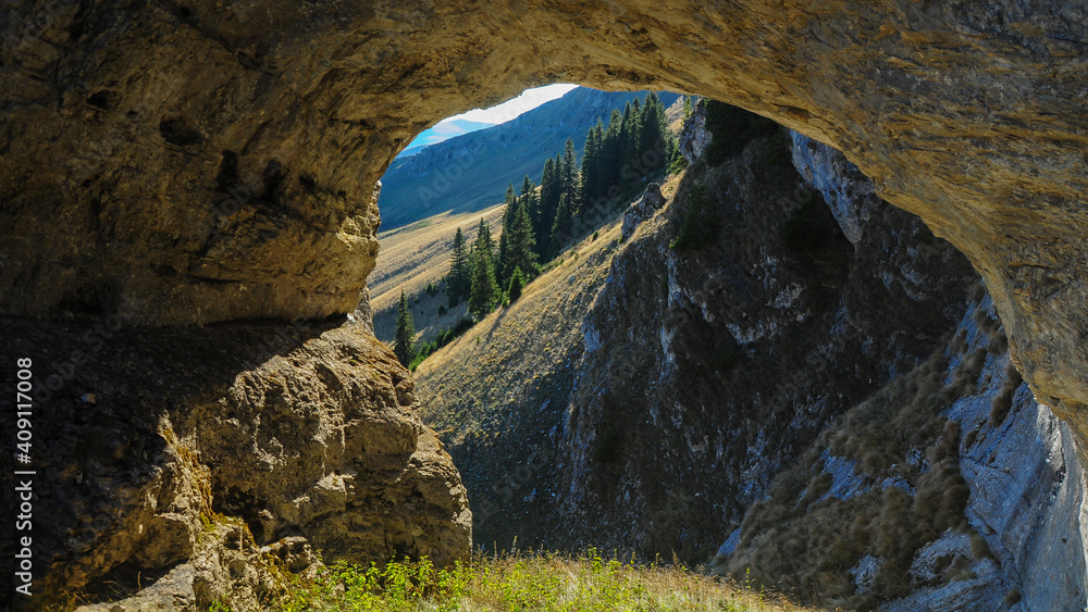 Obraz premium An arched cave eroded in a calcareous cliff located on top of Latorita mountains. The formation opens to a mountainous view: the grassy crests of Fratosteanu Peak. Carpathia, Romania.
