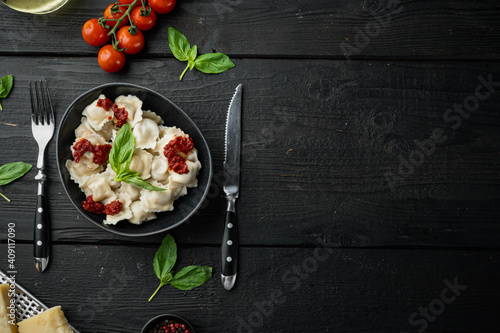 Appetizing ravioli with tomato sauce, cheese and basil with basil parmesan and tomatoe in black bowl, on black wooden table background , top view flat lay , with copyspace  and space for text