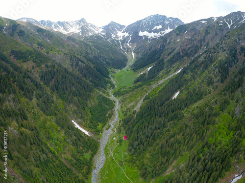 Aerial drone panorama of an alpine valley narrowed by the rocky ridges of Fagaras Mountains. Spring season, The mountain peaks are still covered in snow. Carpathia, Romania.