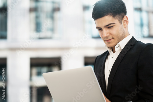 Prints a text to its director about the work done on the project. a businessman of Indian appearance works on a laptop computer in a black business suit.