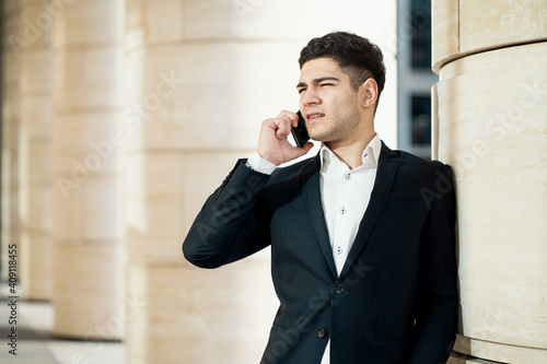 the financier manager is talking on the phone with a colleague partner, holding a laptop in their hands. He is dressed in a black business suit and a white shirt. male of European appearance ethnics.