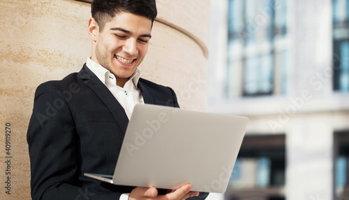 a man in a business suit is working on a laptop, typing a message to a partner. Dark-haired Indian appearance. Does his work near the business center.