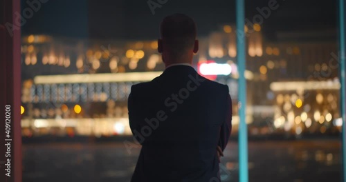 Back view of successful young businessman in suit is looking out of panoramic window.