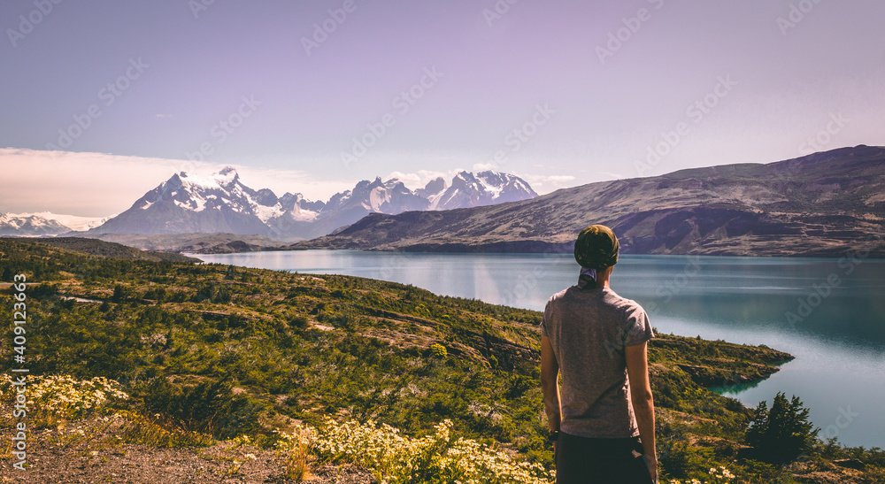 Fototapeta premium Person standing viewing a lake and mountains with snow from a hill. Torres del Paine national park, Patagonia, Chile, South America