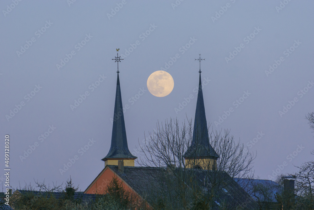 Fototapeta premium Full moon in between two church towers in the blue evening sky