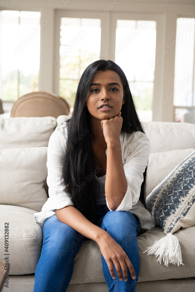 Stern, worried looking Indian woman sitting on the couch in a farmhouse-style home Stern, worried looking Indian woman sitting on the couch in a farmhouse-style home