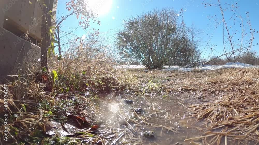 Wide angle closeup of water drops hitting a small puddle after falling from melting snow of the roof; in slow motion with flares from water and sun Wide angle closeup of water drops hitting a small puddle after falling from melting snow of the roof; in slow motion with flares from water and sun