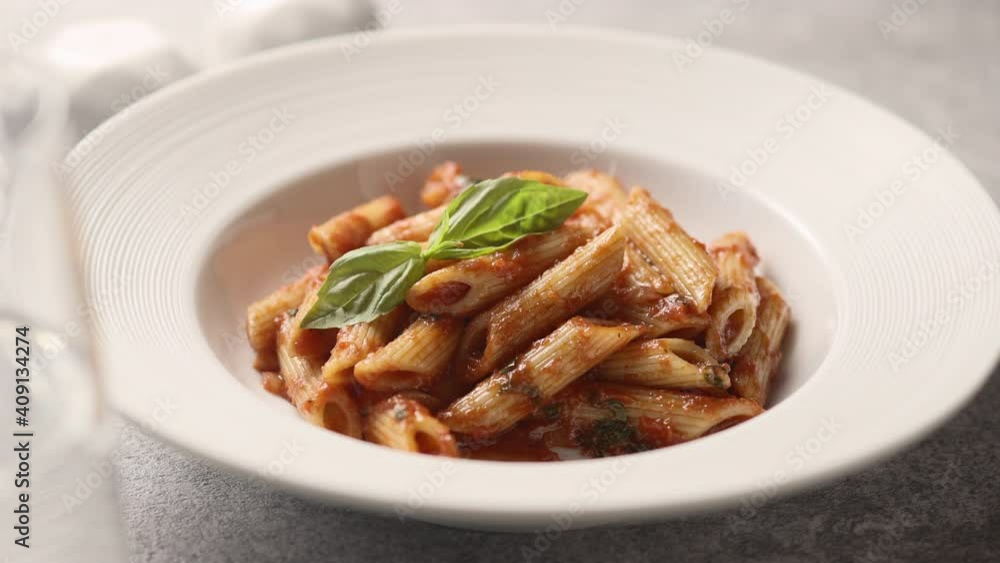 Girl pricks penne pasta with fresh green basil on a fork, close-up Girl pricks penne pasta with fresh green basil on a fork, close-up