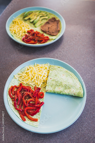 plant-based food, vegan version fo the viral layered tortilla wrap hack with red peppers grated dairy-free cheese avocado and refried beans