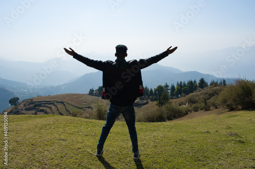 boy on top of green hill with both arms wide open enjoying nature