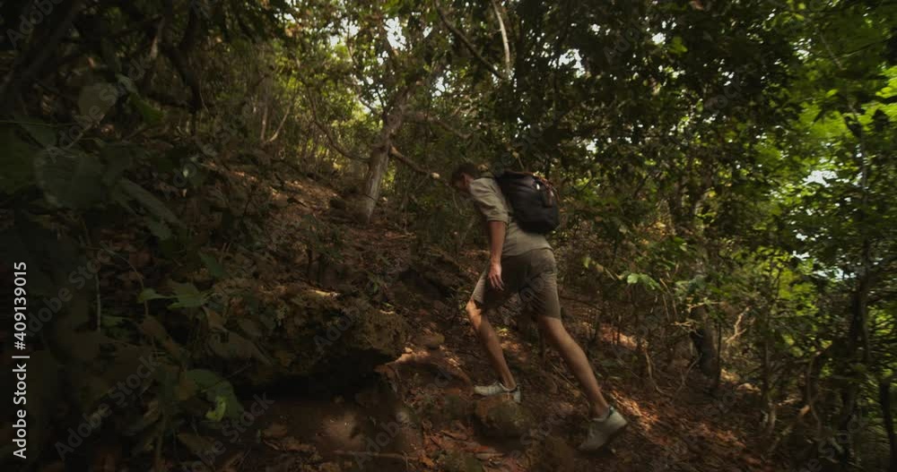 Young white male ascending up the steep hill in tropical rainforest alone. Tourist exploring a tropical jungle in Bali Young white male ascending up the steep hill in tropical rainforest alone. Tourist exploring a tropical jungle in Bali