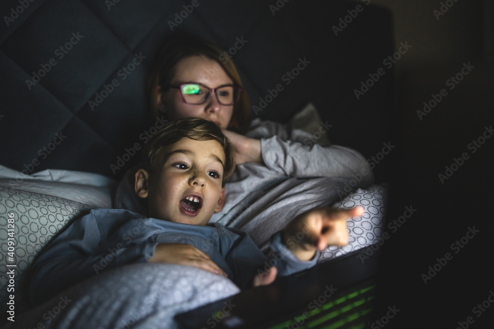 Mother and son watching movie or cartoon using laptop in bed at nighttime - Small boy and his mom using computer while lying in bed at night in dark room - leisure activity family bedtime concept Mother and son watching movie or cartoon using laptop in bed at nighttime - Small boy and his mom using computer while lying in bed at night in dark room - leisure activity family bedtime concept