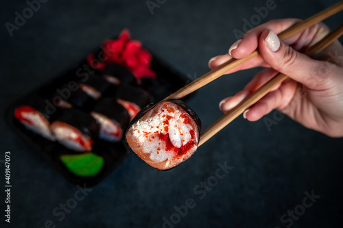 Woman eating delivered sushi from a container with japanese sticks