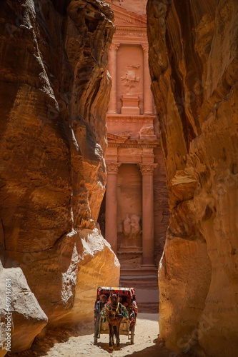 View of Treasury at Petra, Jordan through desert cliffs with a tourist riding horse cart vehicle in the middle