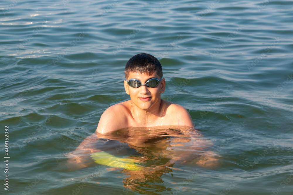 Teenager in goggles swims in the sea with big splashes. Cute boy enjoys swimming in the ocean.  Holidays, vacation with kids