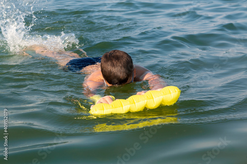 A boy in goggles learns to swim with a yellow inflatable mattress. Teenager in goggles swims in the sea with big splashes. A cute boy enjoys swimming in the ocean.