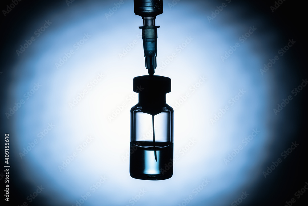 .The Coronavirus Vaccine and Syringe injection on a dark blue background, silhouette. The concept of protection against Coronavirus infection, COVID-19. Healthcare and medical concept. .The Coronavirus Vaccine and Syringe injection on a dark blue background, silhouette. The concept of protection against Coronavirus infection, COVID-19. Healthcare and medical concept.