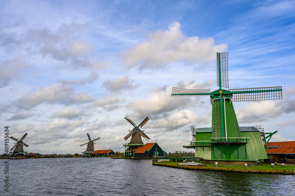 Green windmills and grasslands along the canal on a clear day. Beautiful clouds in Zaanse Schans, Netherlands This is a popular tourist destination.