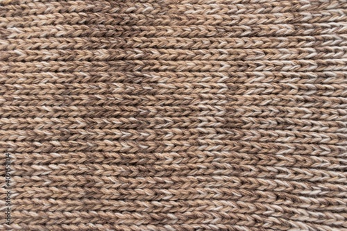 Knitted background. Knitted wallpaper. Beige knitted fabric. Knitted texture. Soft material. Brown  beige and white handmade sweater close up photo. Cozy background. Knitwear detail. Woolen cloth.