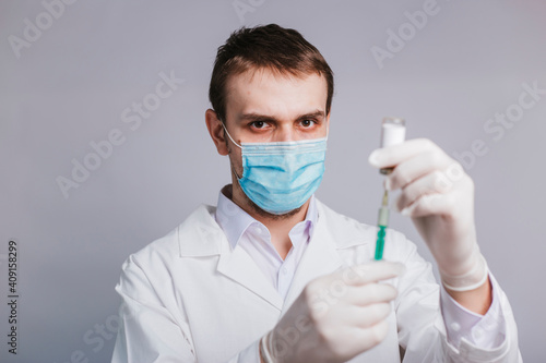 A male doctor in a white coat is taking medicine into a syringe from an ampule. Vaccination and immunization of the population. studio