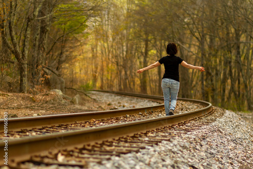 Foto A young caucasian woman wearing jeans and t shirt is walking on the railroad tracks at a rural location with her arms wide open