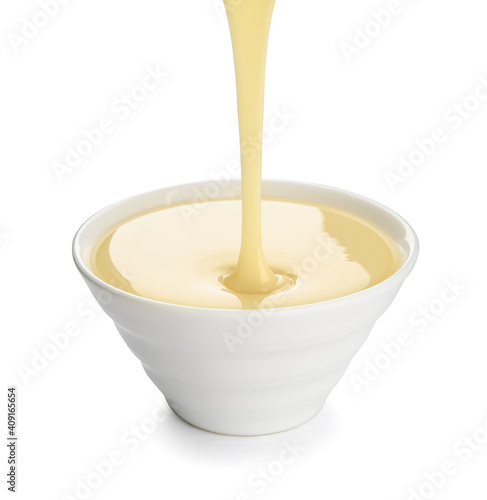 Sweet condensed milk pouring into bowl on white background photo