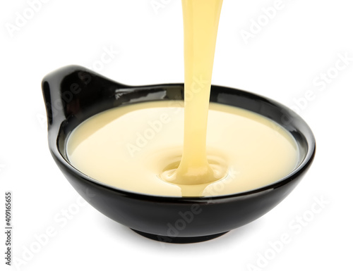 Sweet condensed milk pouring into bowl on white background