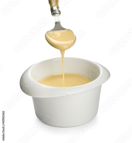 Bowl with sweet condensed milk and spoon on white background
