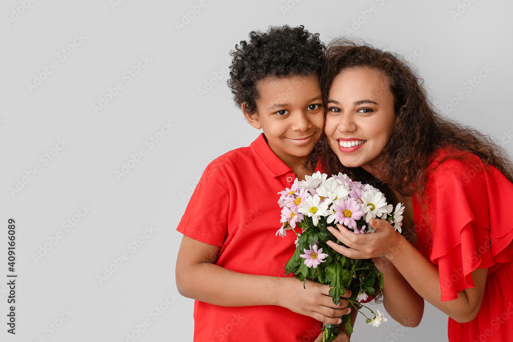 African-American boy and his mother with flowers on grey background African-American boy and his mother with flowers on grey background
