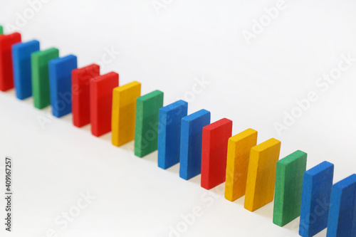 Colored dominoes stand in a row on a white background. A chain reaction dominoes