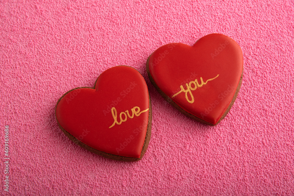 Two red cookies in shape of hearts with the inscription LOVE YOU. Pink background.
