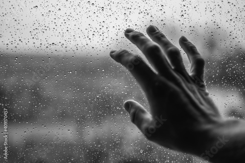 Hand an einer vom Regen benässten Fensterscheibe mit Blick nach draußen photo