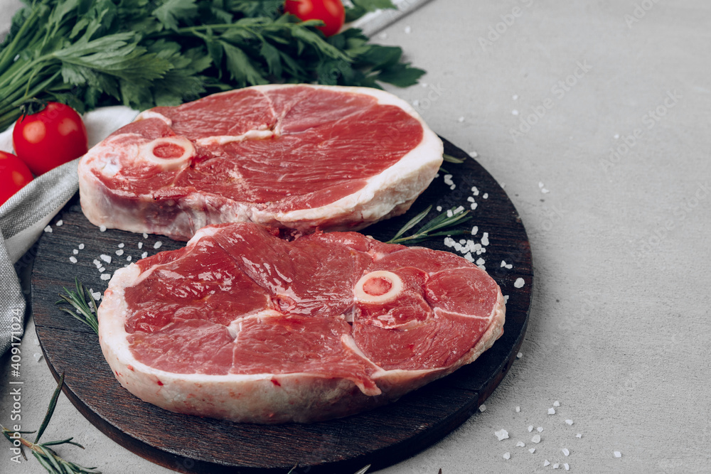 Raw rib-eye beef steak on wooden cutting board on gray background