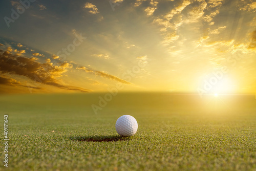white golf ball on green grass at golf course ,sunlight ray blur green background.
