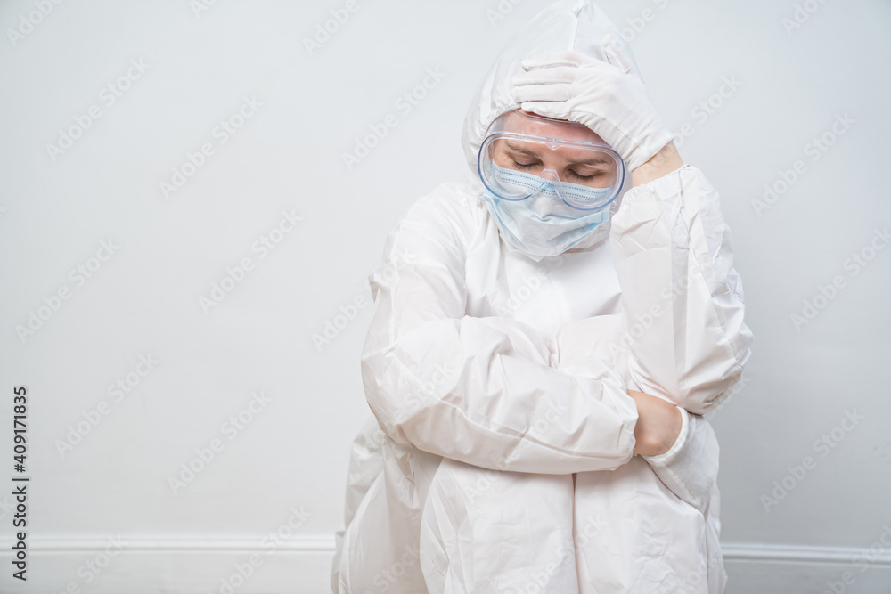 portrait of a tired woman doctor in a protective suit, glasses, mask and glove against the white wall. the hard, dangerous and responsible work of medics during the pandemic. coronavirus in the world. portrait of a tired woman doctor in a protective suit, glasses, mask and glove against the white wall. the hard, dangerous and responsible work of medics during the pandemic. coronavirus in the world.