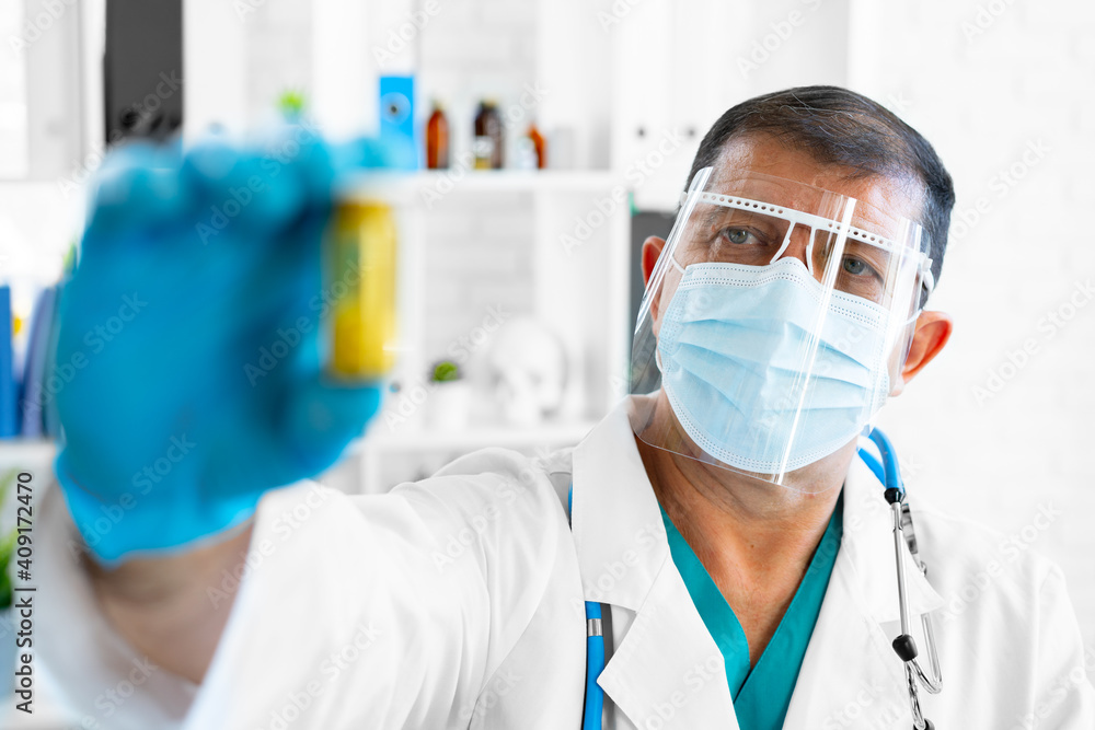 Senior male doctor in mask holding glass jar with medicine Senior male doctor in mask holding glass jar with medicine