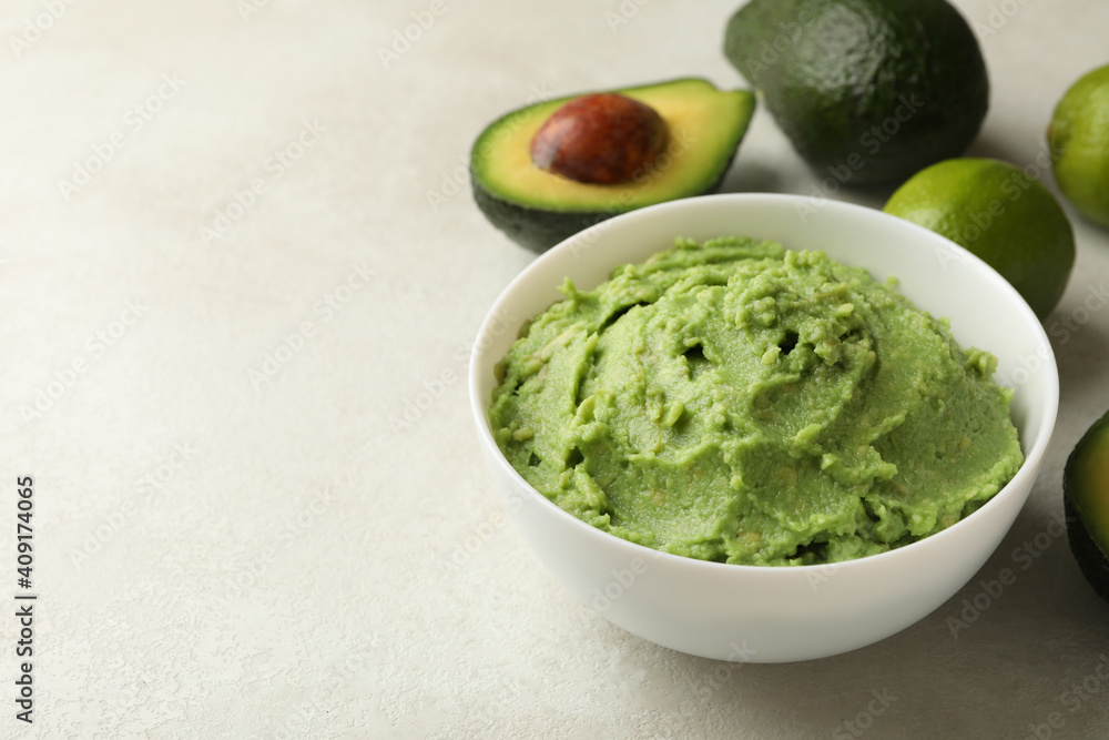 Bowl of guacamole, avocado and lime on white textured background, space for text Bowl of guacamole, avocado and lime on white textured background, space for text