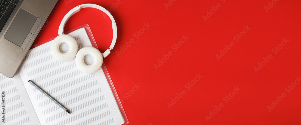 Top view open music book, headphones pen and laptop on red background. workplace. banner