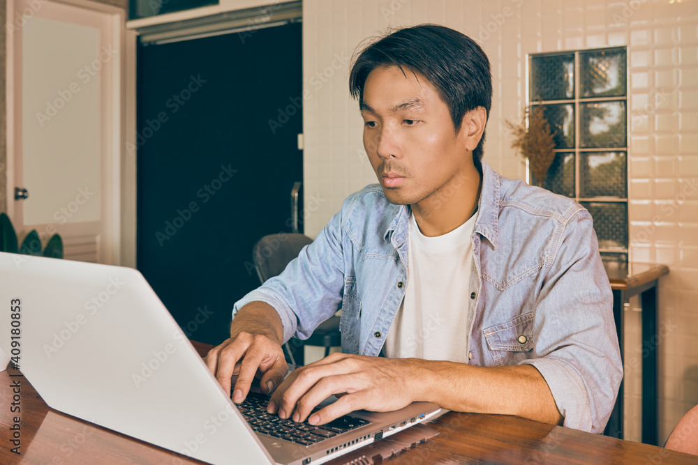 Zoom View Front Left Asian Casual Businessman in Denim or Jeans Shirt Typing Laptop in Coffee Shop. Casual Businessman with Technology in Vintage Tone Zoom View Front Left Asian Casual Businessman in Denim or Jeans Shirt Typing Laptop in Coffee Shop. Casual Businessman with Technology in Vintage Tone