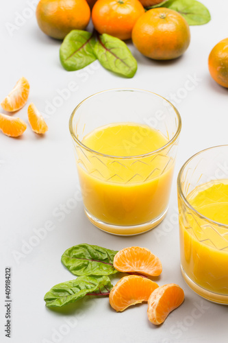 Citrus fruit juice in glasses. Tangerine slices with leaves on table