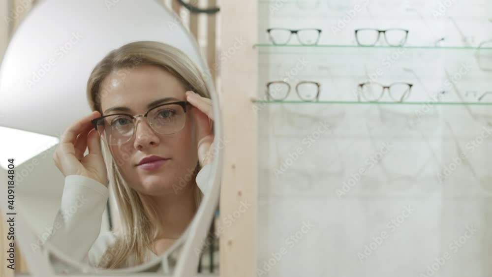 Lockdown of reflection of young Caucasian woman with blond hair trying on fashionable glasses in optician store Lockdown of reflection of young Caucasian woman with blond hair trying on fashionable glasses in optician store