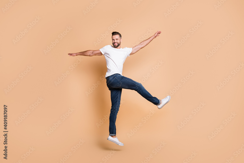 Full length body size view of attractive funky cheerful guy jumping having fun dancing isolated over beige pastel color background Full length body size view of attractive funky cheerful guy jumping having fun dancing isolated over beige pastel color background