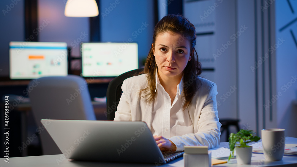 Tired woman manager raising head looking at camera sighing after typing on laptop, working late at night in start-up business office. Focused employee using technology network wireless doing overtime Tired woman manager raising head looking at camera sighing after typing on laptop, working late at night in start-up business office. Focused employee using technology network wireless doing overtime