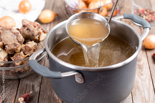 Saucepan with bouillon with a ladle on a wooden table. Bone broth photo