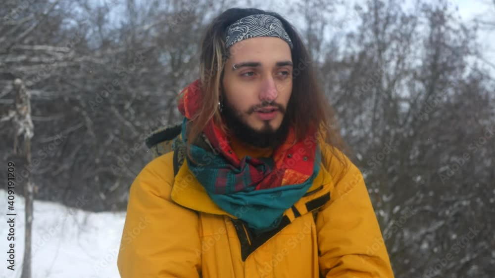 Young twenty-year-old guy traveler walks in a snowy forest in the mountains, snowflakes are falling around Young twenty-year-old guy traveler walks in a snowy forest in the mountains, snowflakes are falling around