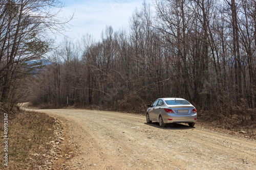 The car is on a dirt road that goes around a bend in the unknown. A rocky clay road in the Russian forest in spring.