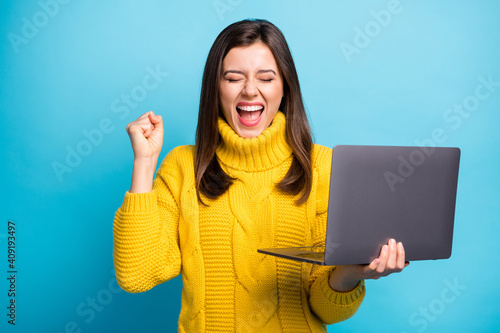 Close-up portrait of lovely cheerful girl holding in hands laptop celebrating breakthrough isolated over shine blue color background