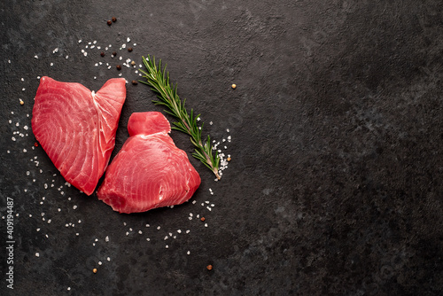 Fresh raw tuna steaks with rosemary and spices on a stone background with copy space for your text